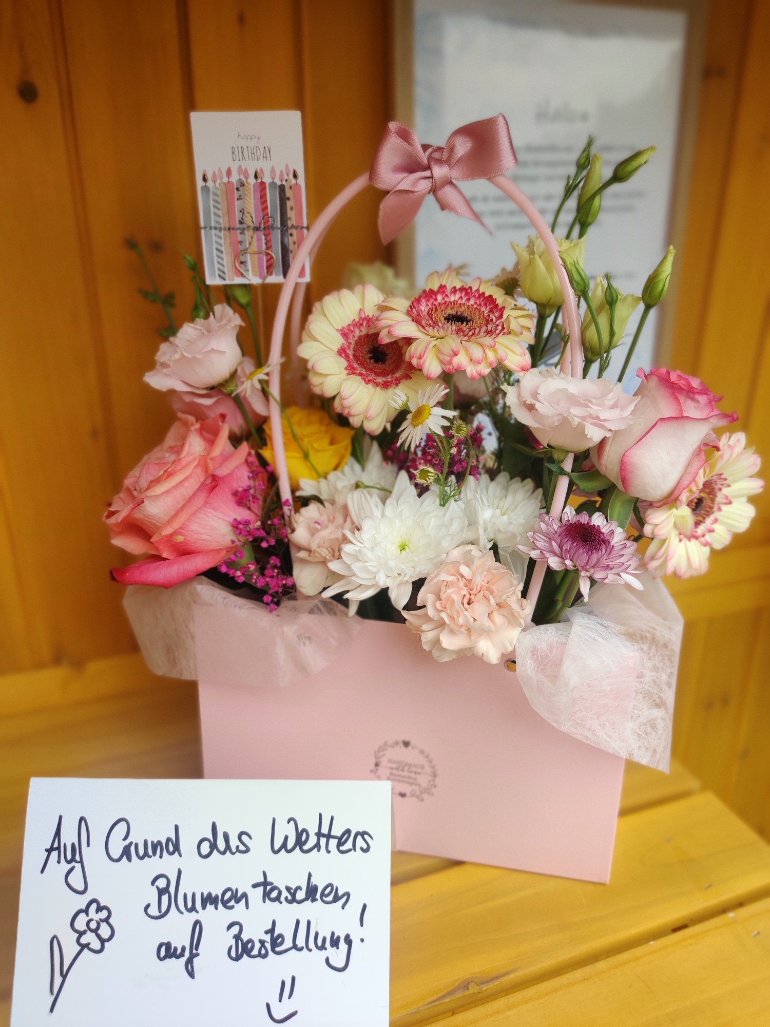 Rosa Blumentasche mit rosa Schleife und Geburtstagskarte, davor ein Schild: Auf Grund des Wetters Blumentaschen auf Bestellung