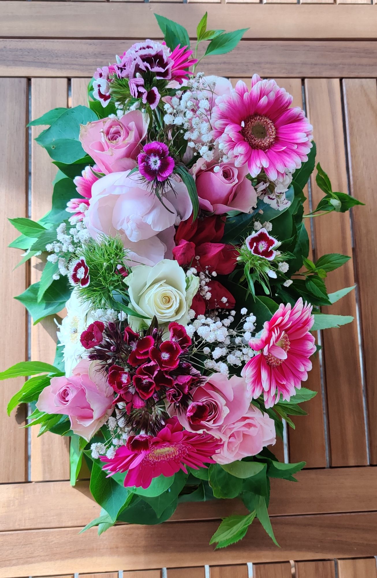 Langes Tischgesteck mit rosa Rosen, Gerbera, Bartnelken und Schleierkraut auf einem Holztisch